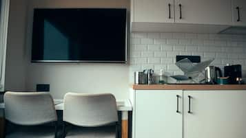 A modern kitchen with white cabinets, a large flat-screen TV, and a dining area with two chairs.