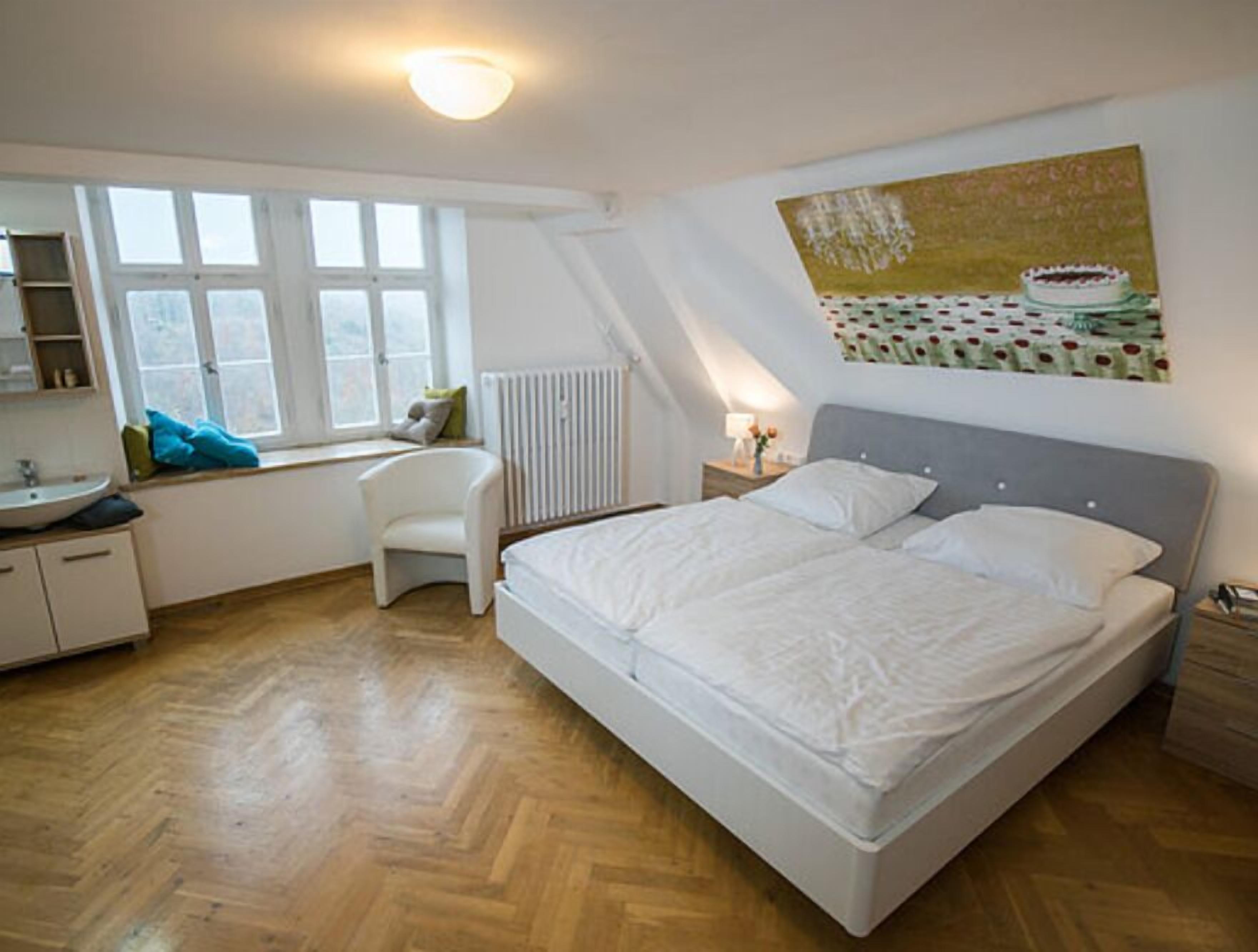 Een slaapkamer met een bed, raam, radiator, stoel en nachtkastje.