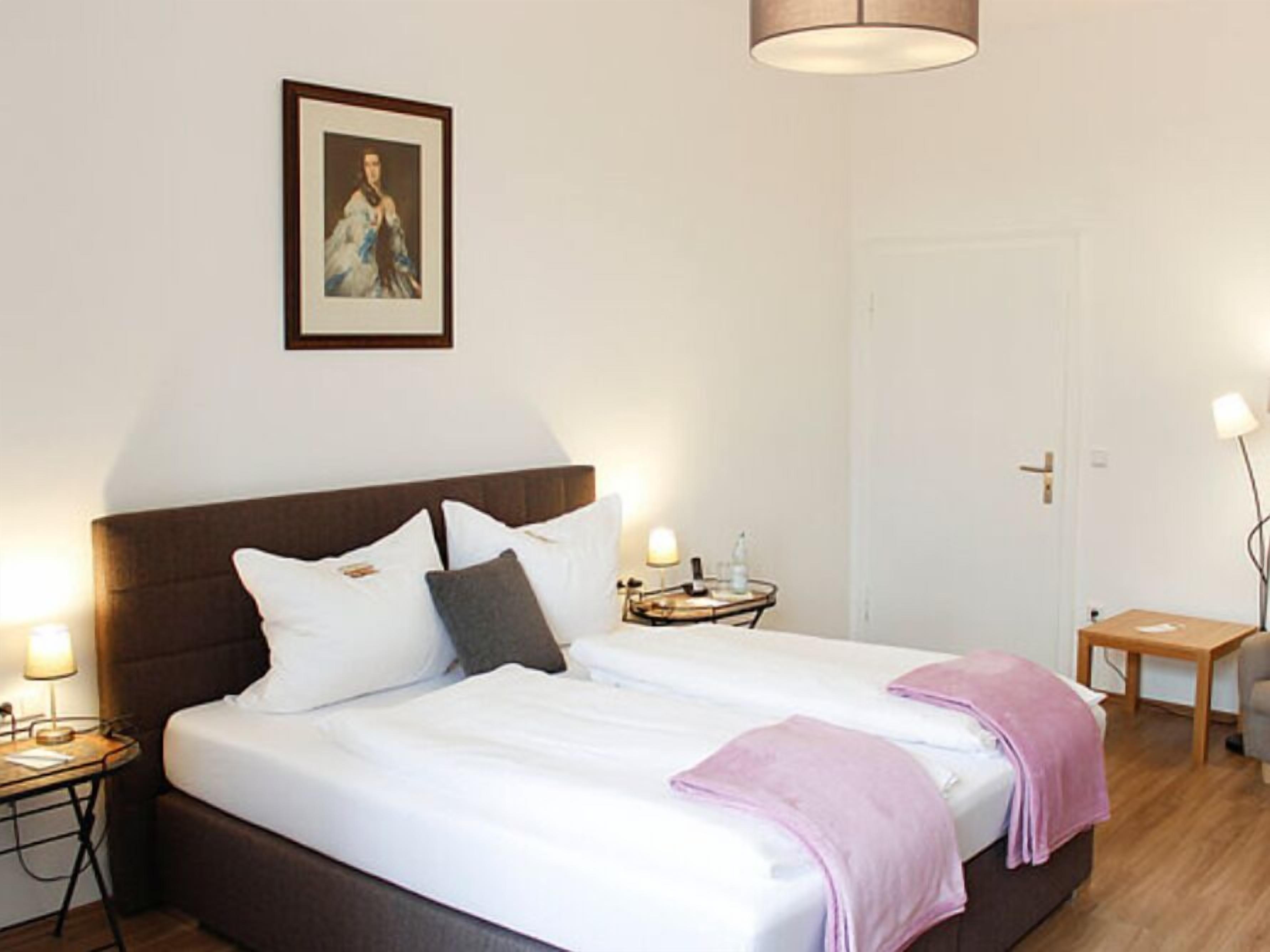 Une chambre d’hôtel bien rangée, avec un grand lit, des tables de chevet, une lampe de chevet et un tableau encadré au mur.