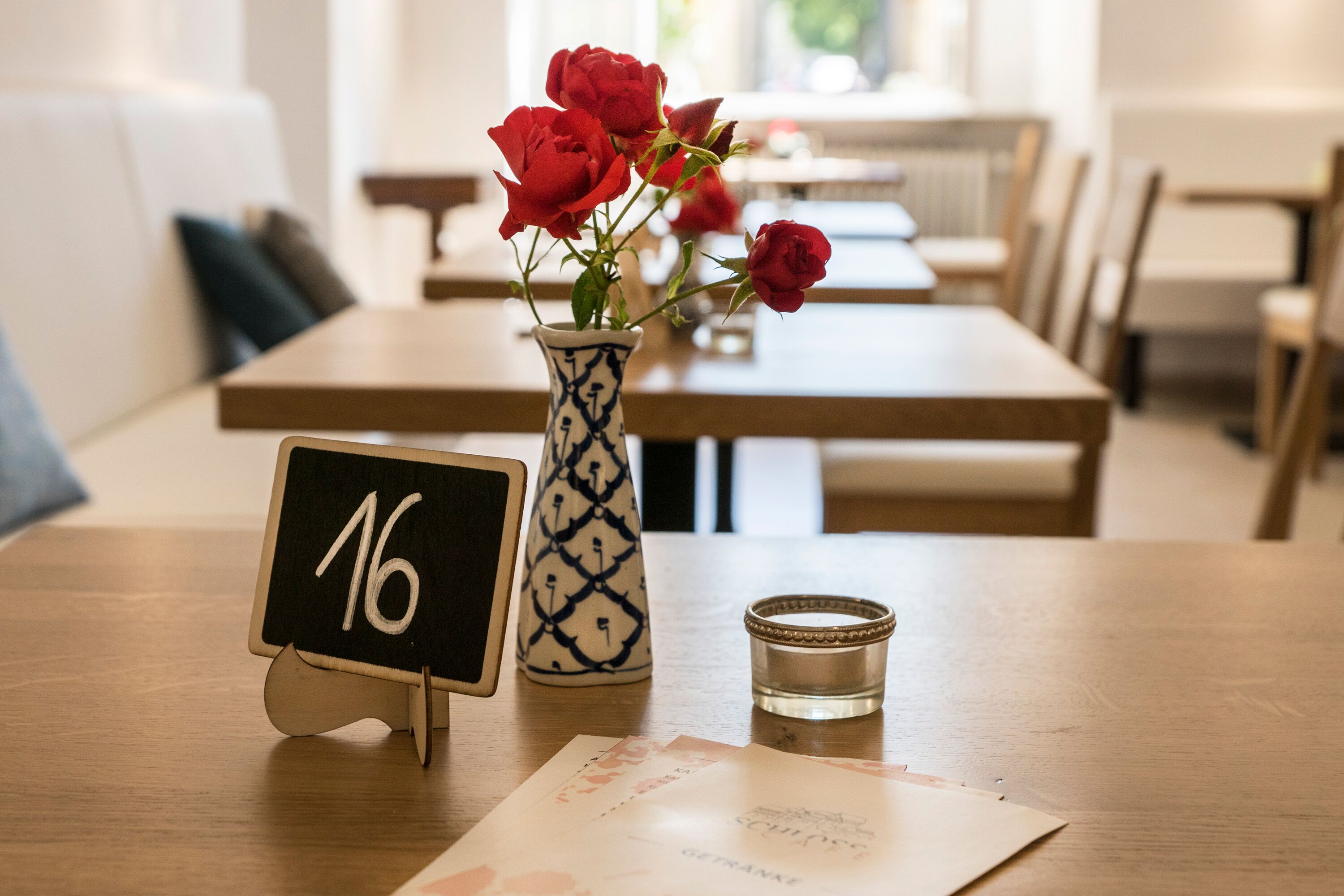 A dining table with a vase of red roses, a candle, and a blackboard with the number 16.