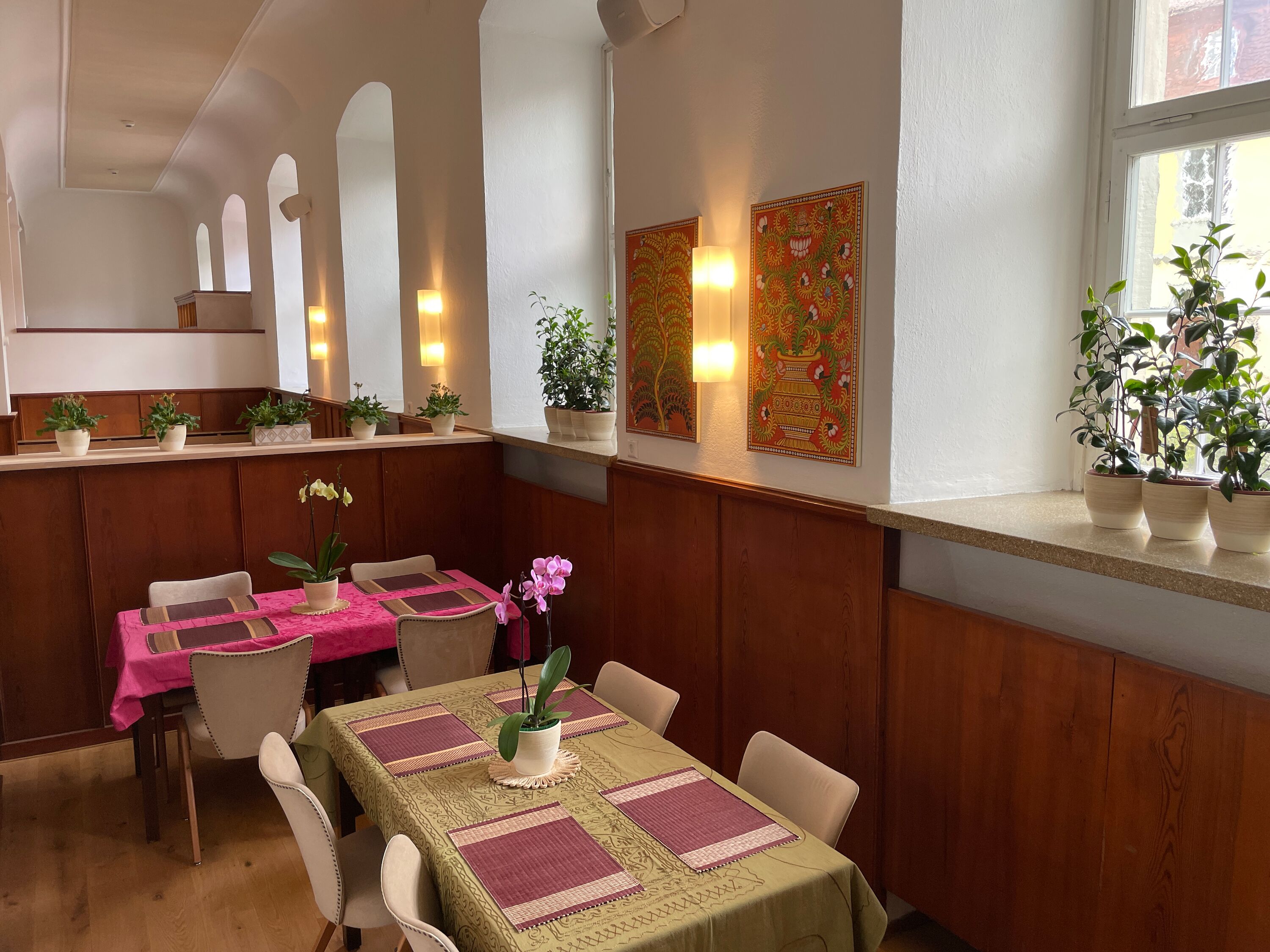 Un restaurante con paneles de madera, una mesa con mantel rosa y plantas en macetas en el alféizar.