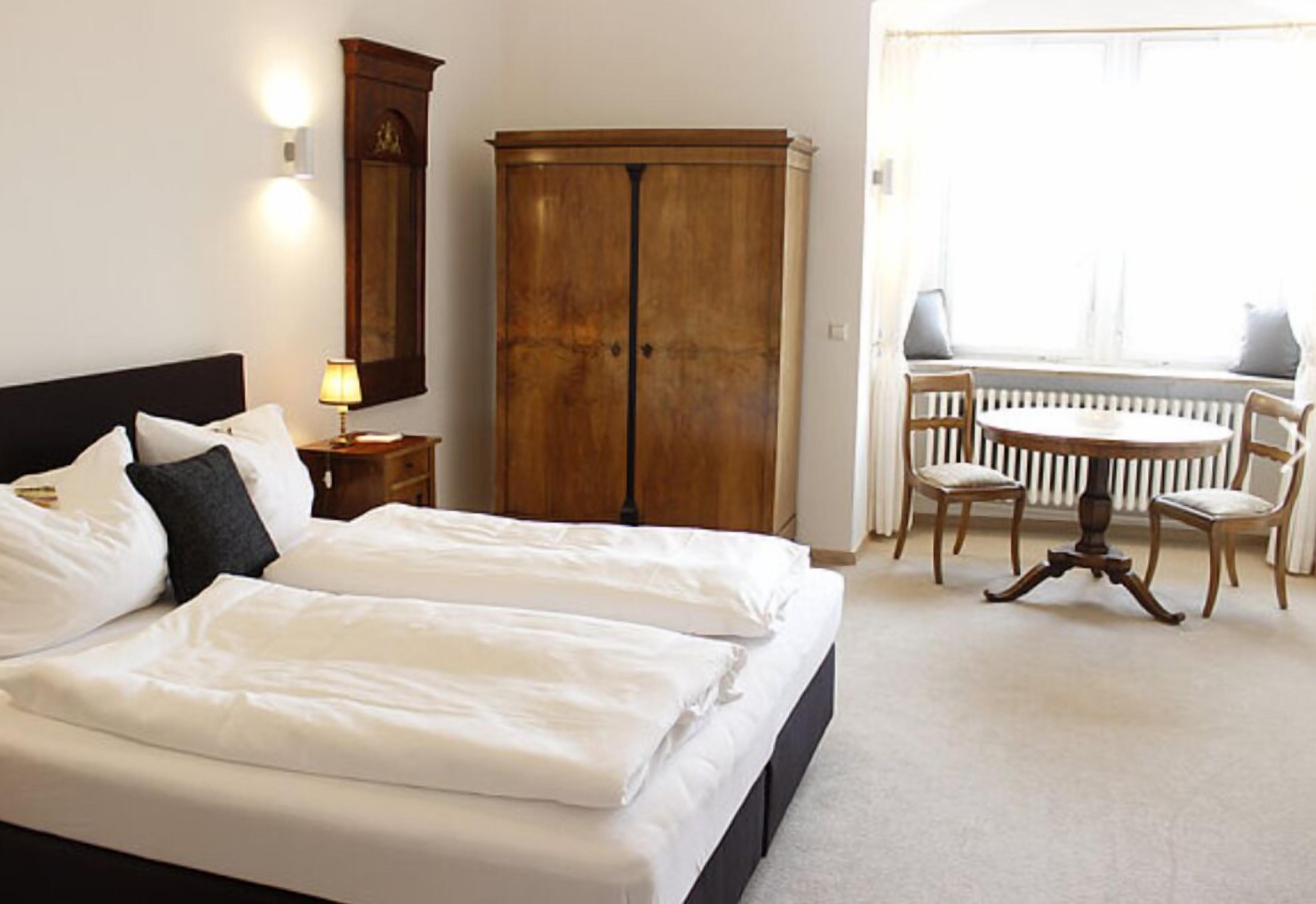 Ein Hotelzimmer mit einem großen Bett, einem Holzschrank, einem runden Tisch mit Stühlen und einem Fenster mit Blick ins Freie.