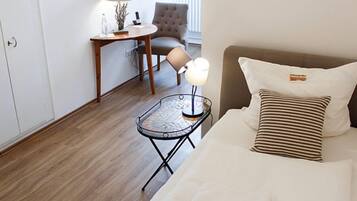 Ein Hotelzimmer mit Bett, Nachttisch mit Lampe, Sessel und kleinem Tisch ebenfalls mit Lampe.