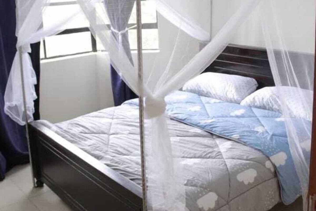 A bed with a canopy, a window with curtains, and a tiled floor.