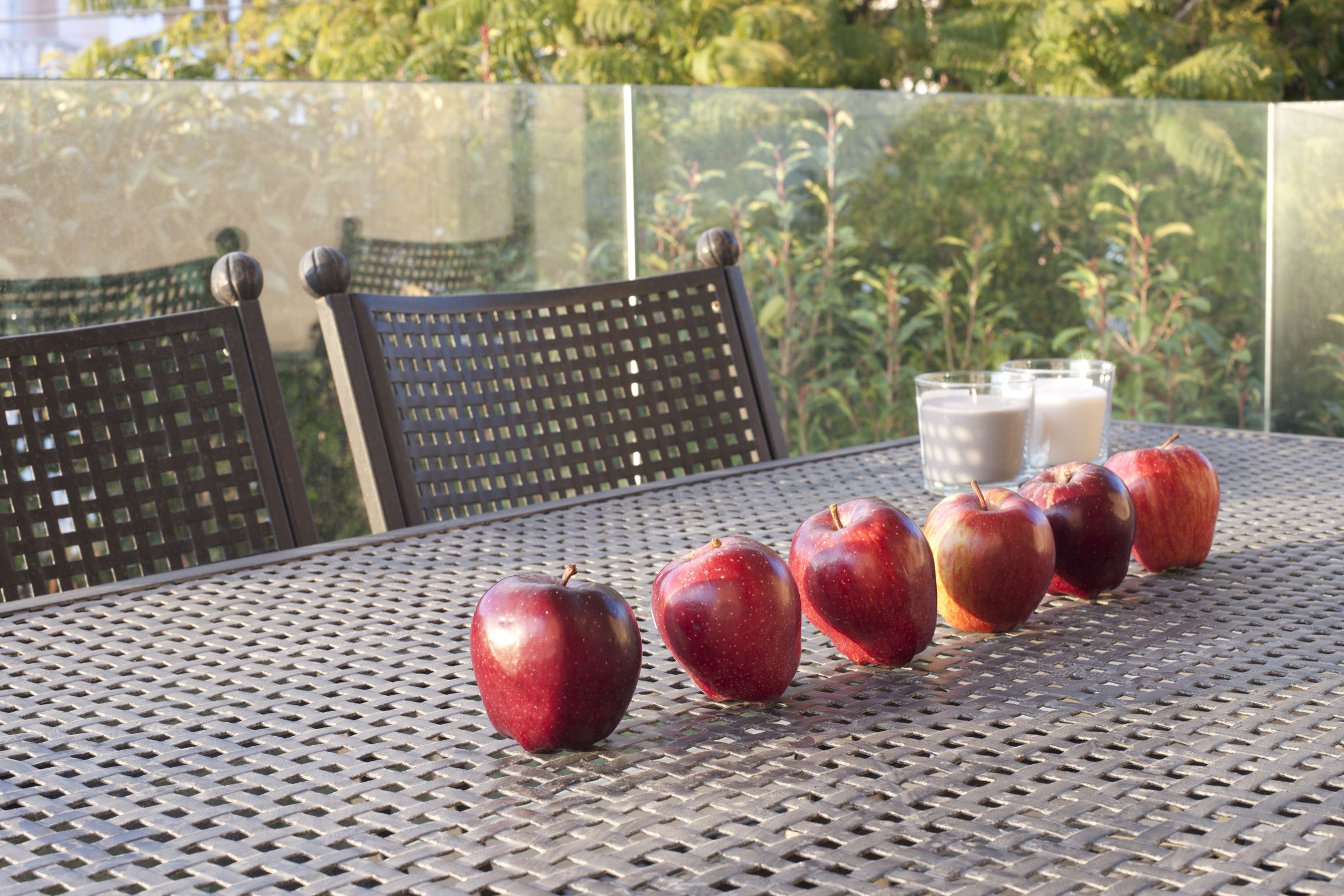 Uma mesa com maçãs e copos de leite, uma cadeira e um muro de vidro ao fundo.