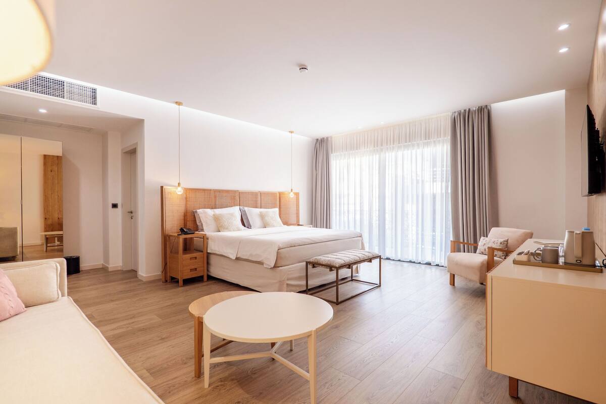 Moderni hotellihuone, jossa on sänky, yöpöytä, tuoli, pyöreä pöytä ja televisio.