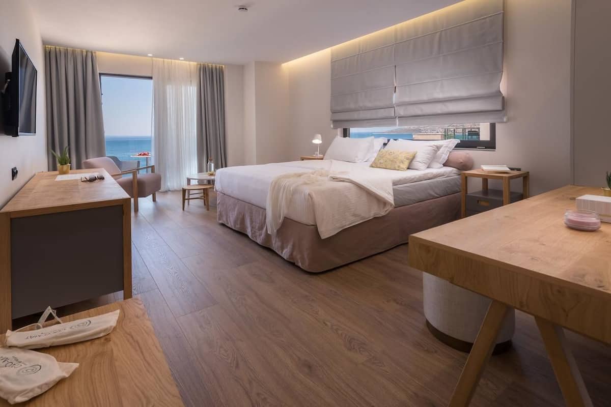 Moderni hotellihuone, jossa on suuri sänky, työpöytä ja näkymä merelle.