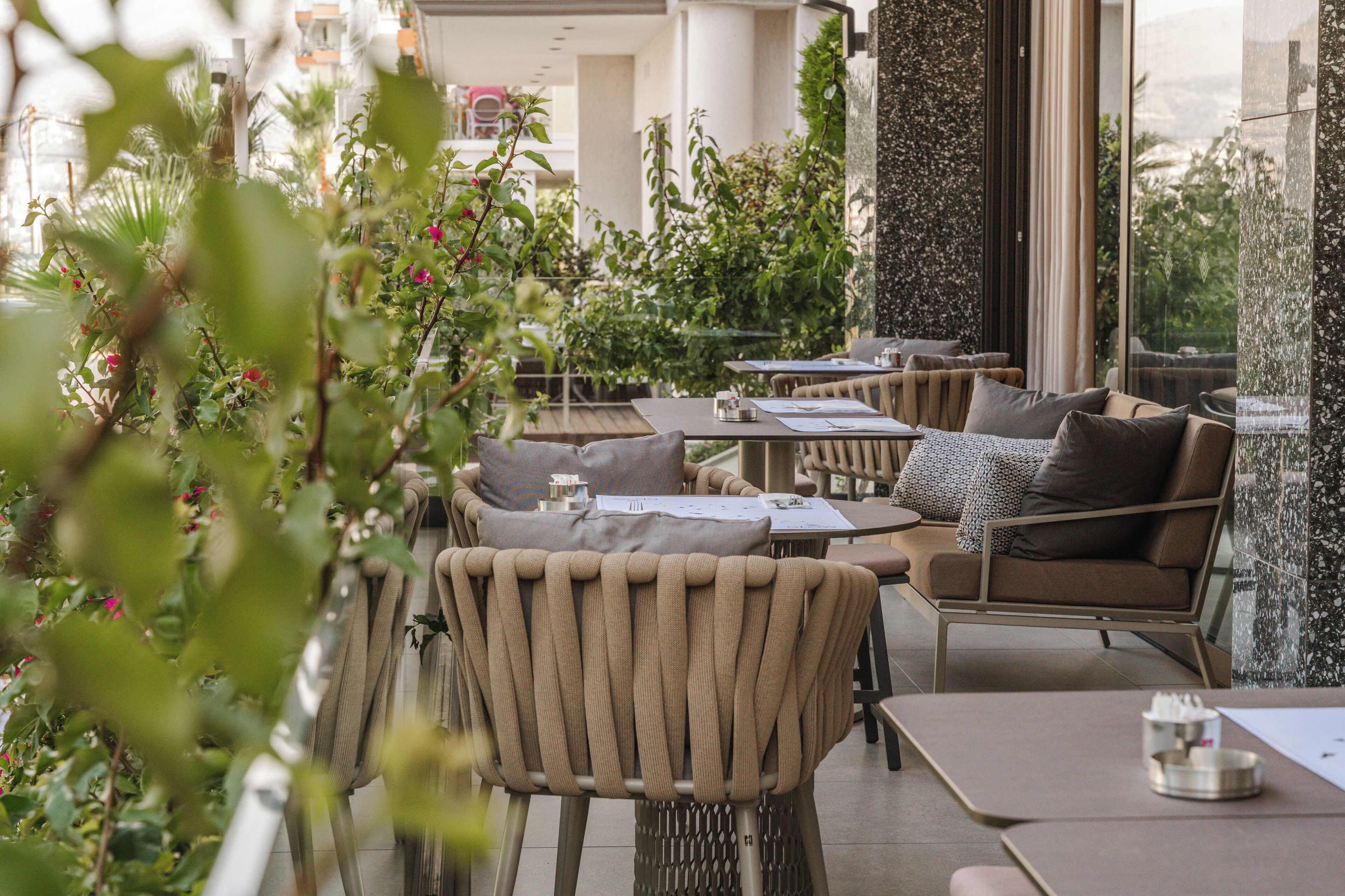 An outdoor seating area with tables and chairs, surrounded by greenery and a view of the cityscape.