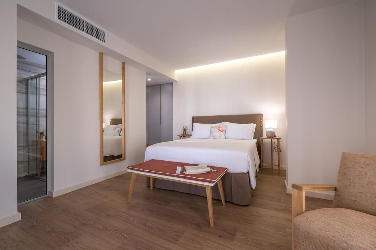 Moderni hotellihuone, jossa on suuri sänky, yöpöydät, peili ja puulattia.