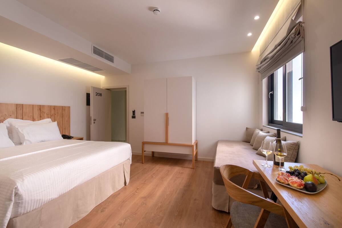Hotellihuone, jossa on suuri sänky, työpöytä tuolilla, pieni pöytä ruokaa ja juomia varten sekä ikkuna, jossa on verhot.
