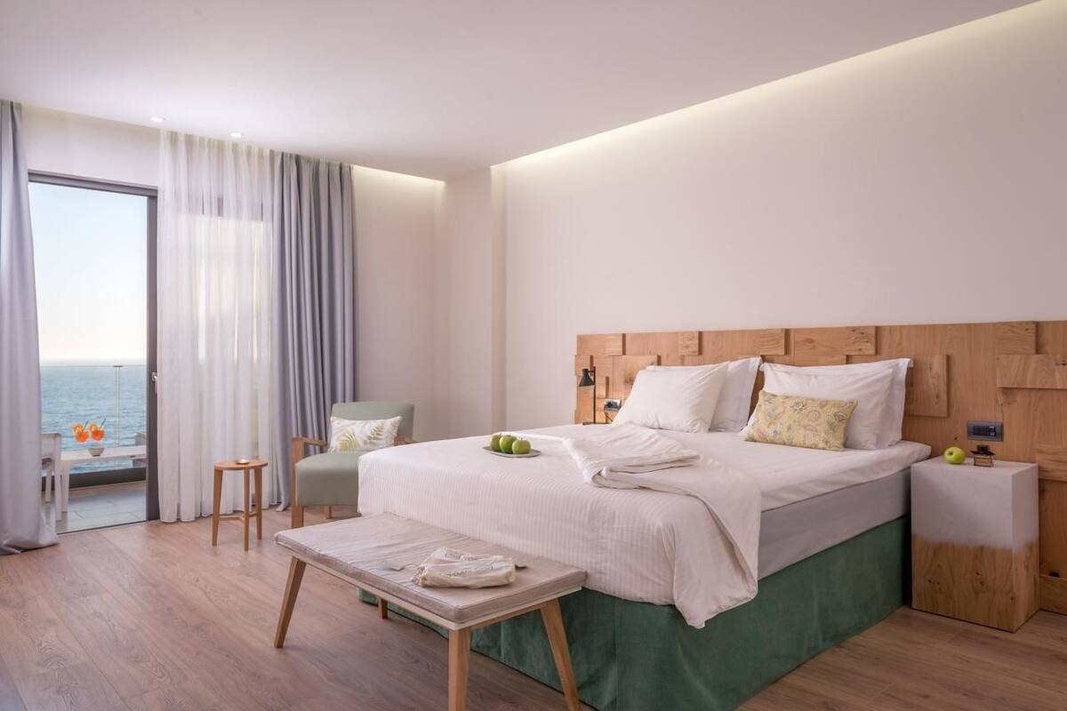 Moderni hotellihuone, jossa on suuri sänky, pieni pöytä, tuoli ja näkymä merelle.