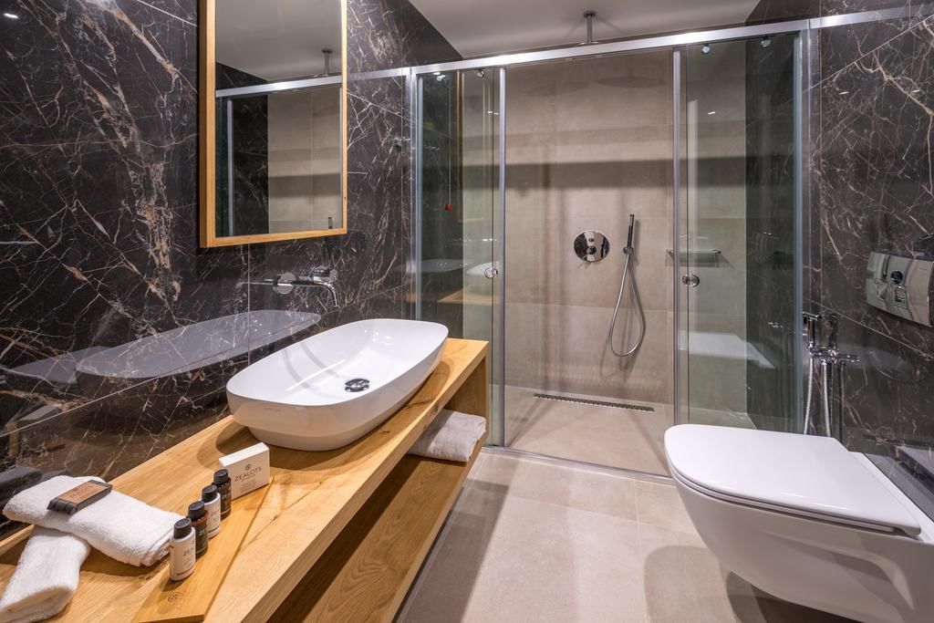 Un baño moderno con un lavamanos grande de mármol, una ducha con mampara de vidrio y un mueble de tocador de madera.