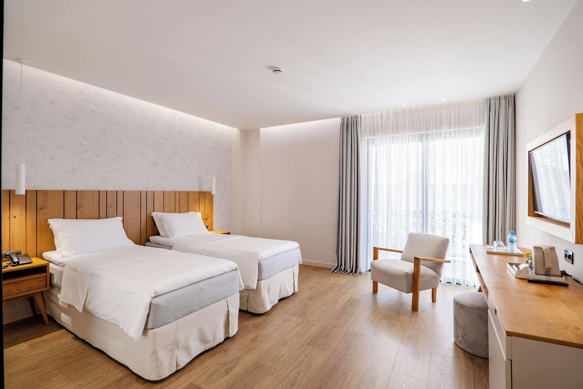 Hotellihuone, jossa on kaksi sänkyä, työpöytä, tuoli, yöpöytä ja ikkuna, jossa on verhot.