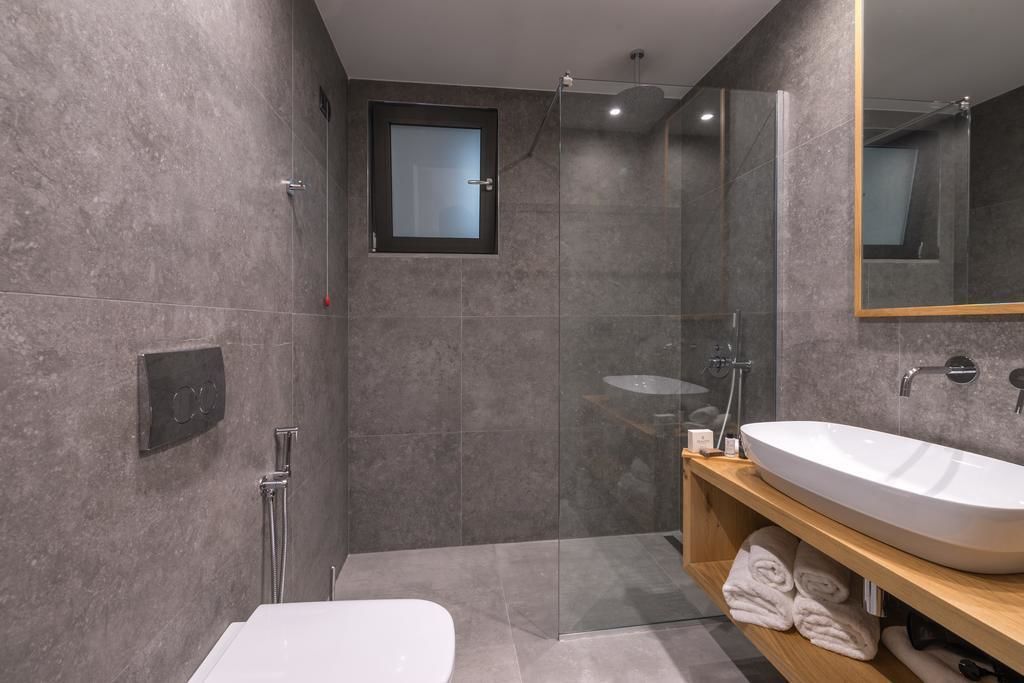 A modern bathroom with a large white sink, a glass-enclosed shower, and a small window.