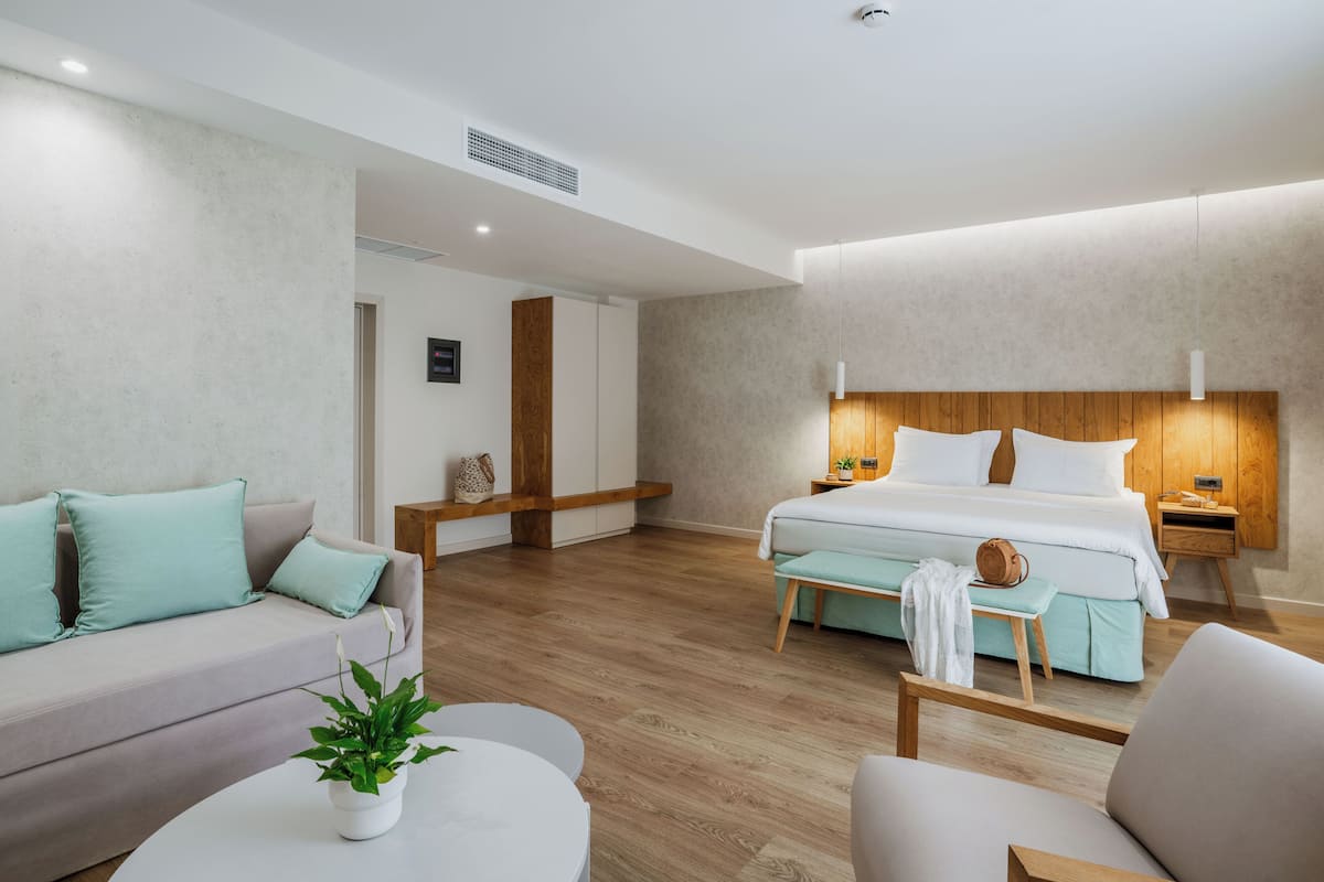 Moderni hotellihuone, jossa on sänky, sohva ja pieni pöytä, jonka päällä on kasvi.