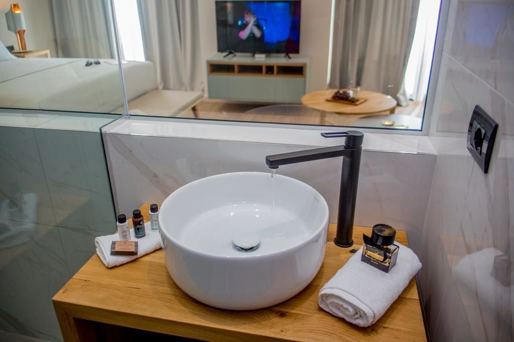 A modern bathroom with a large white sink, a black faucet, and a mirror above it. There are toiletries on the sink and a towel on the side.