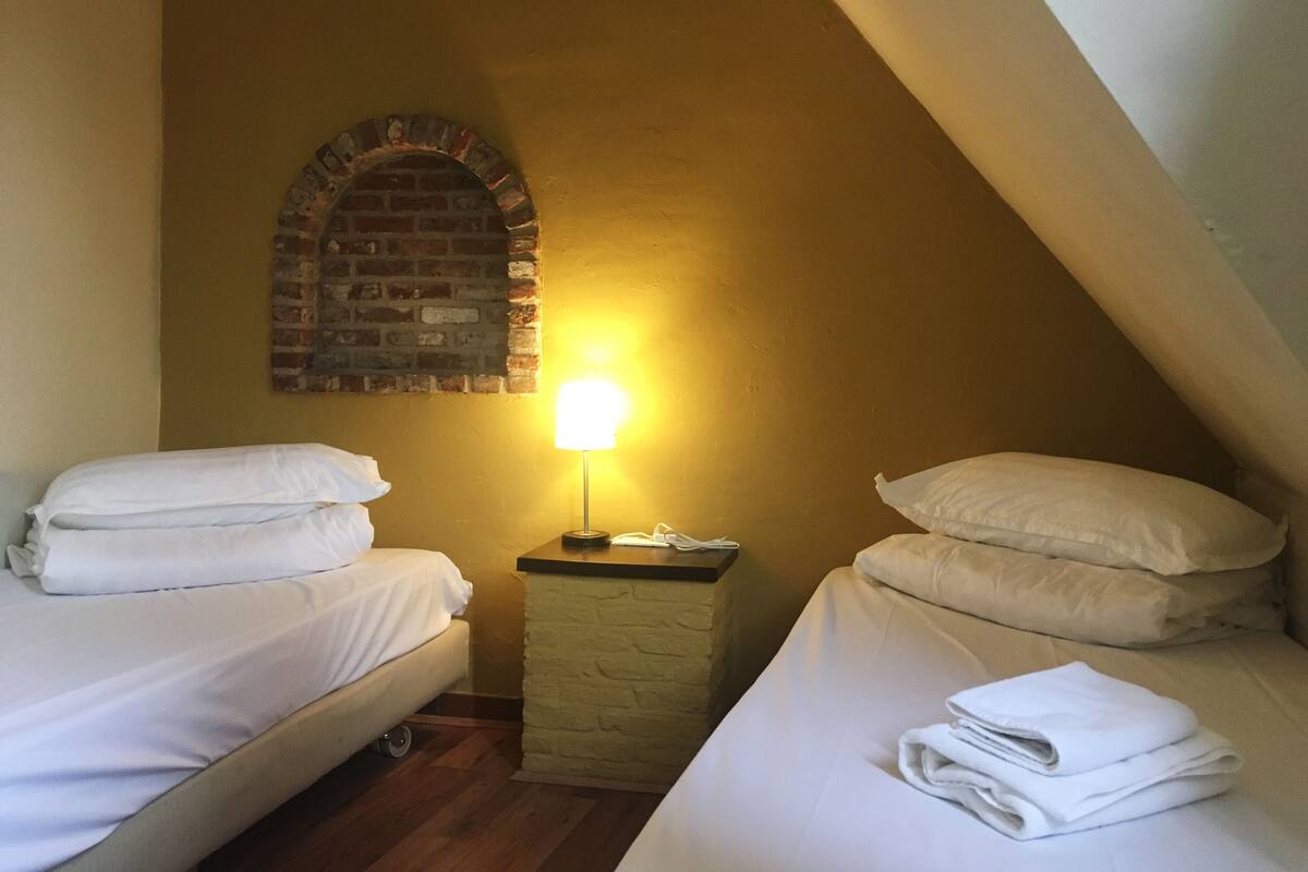 A small, cozy room with two beds, a brick wall arch, and a nightstand with a lamp.