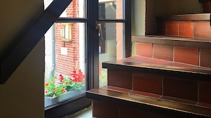 A staircase with red brick steps leading to a landing. A window with a black frame and a glass door is visible, offering a view of a brick building outside. - Hotel Leopold (Bruges)