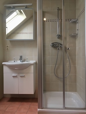 A bathroom with a glass-enclosed shower, a white sink with a mirror above it, and a tiled floor.
