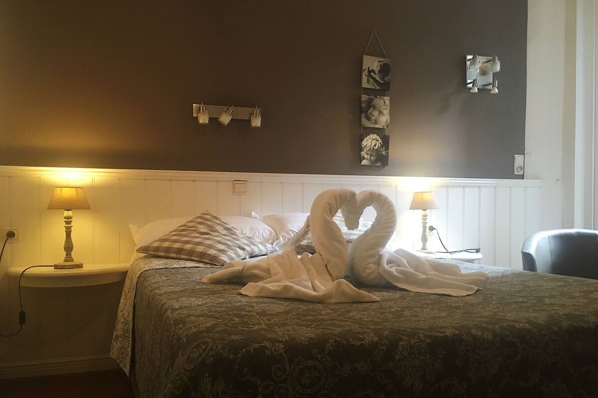 A hotel room with a bed, two bedside lamps, a wall-mounted mirror, and a decorative item above the mirror.