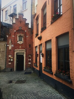 A narrow cobblestone street with a red brick building featuring a black door and a sign reading "Ave Maria". - Hotel Leopold (Bruges)