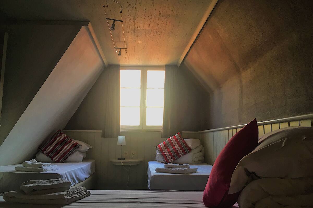 A small, dimly lit attic bedroom with two beds, a window, and a sloped ceiling.