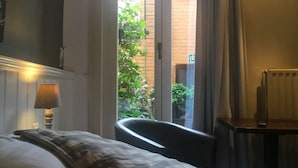 A hotel room with a bed, a chair, a lamp, and a view of the outside. - Hotel Leopold (Bruges)