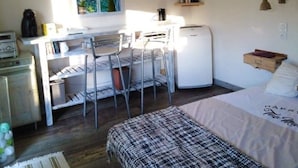 Una habitación pequeña y acogedora con cama, escritorio y silla. Hay una ventana con vistas al verde exterior.