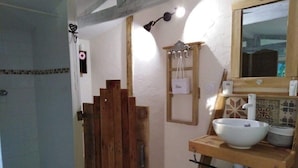 Un baño con puerta de madera, un lavamanos con espejo y un perchero para toallas.