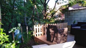Una terraza de madera con una silla y un sofá blancos, rodeada de follaje y una valla de madera.