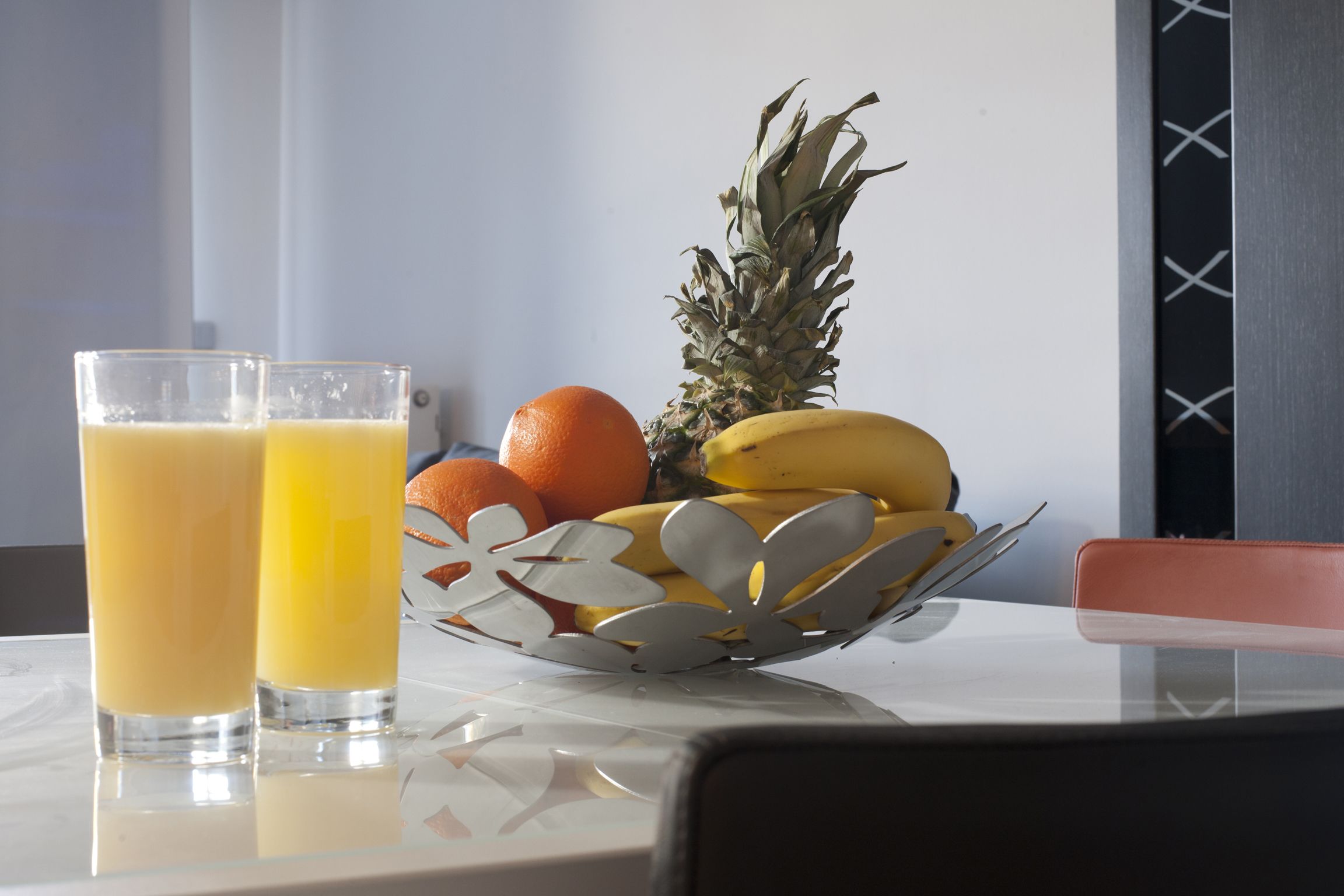 Una mesa con dos vasos de jugo de naranja, una piña, plátanos y naranjas.