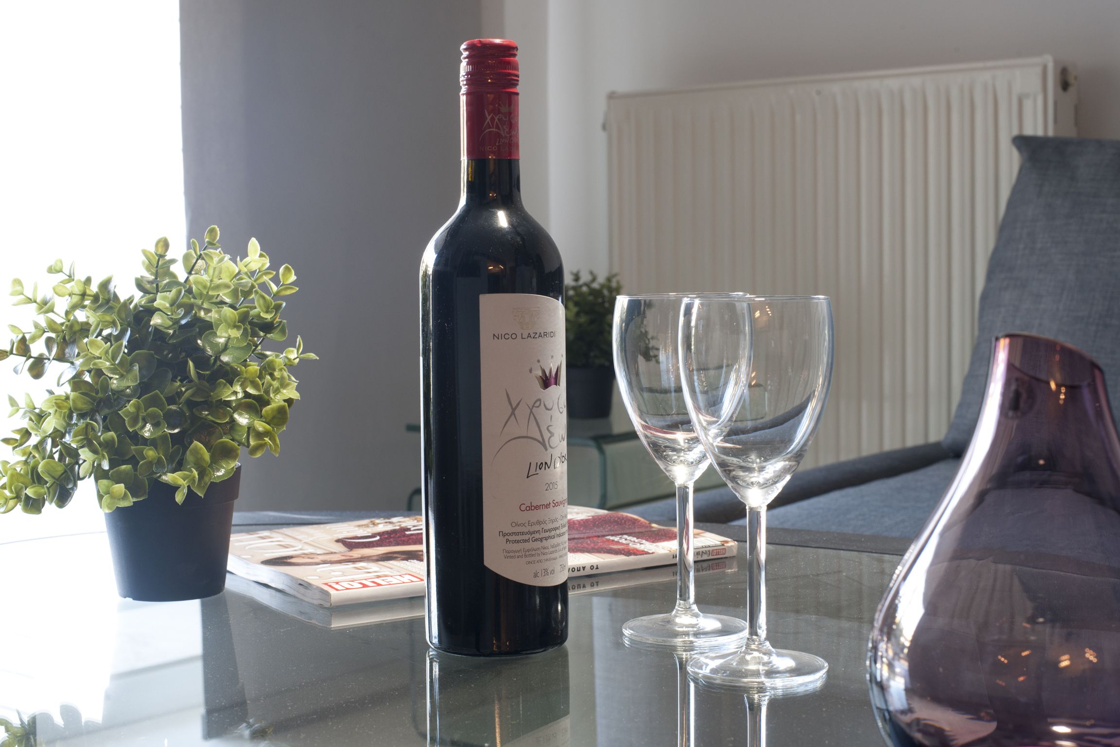 Une bouteille de vin, deux verres et une plante en pot sur une table.