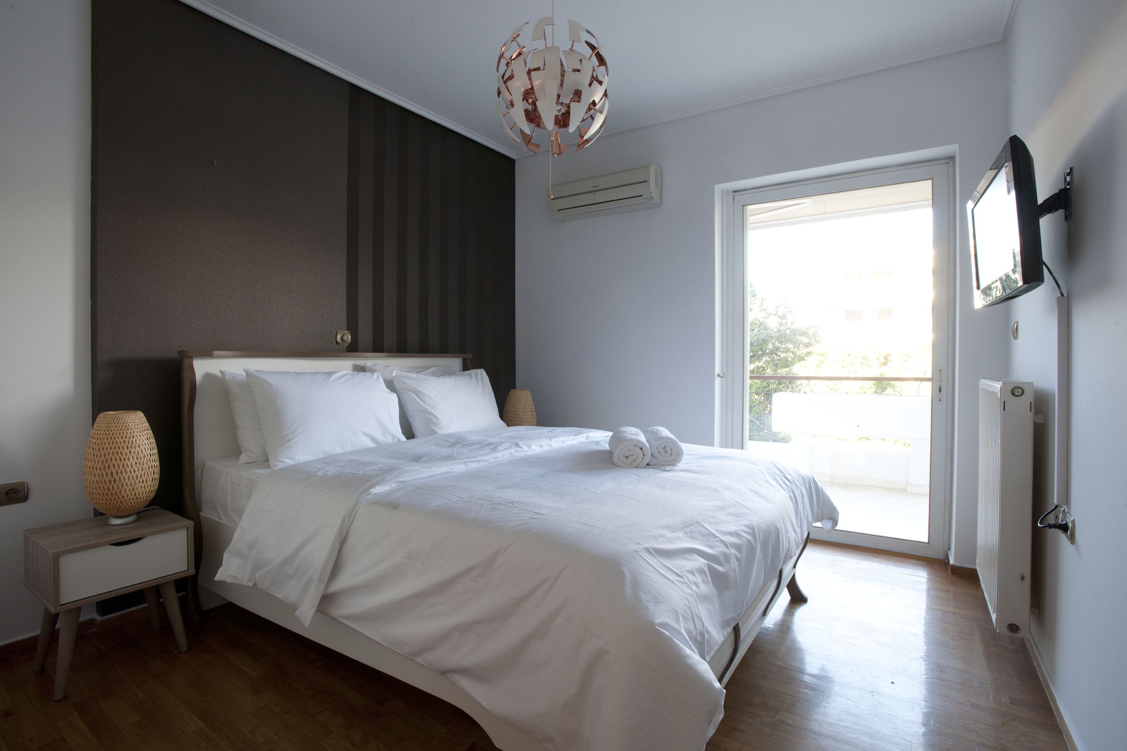 Une chambre à coucher avec un lit, une table de chevet, une lampe et une vue sur l’extérieur.