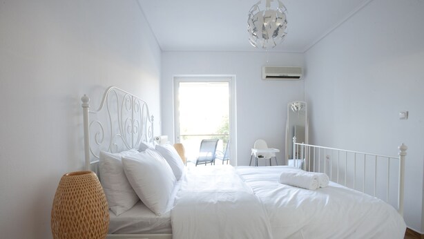 Un dormitorio con una cama blanca, una lámpara de noche, un espejo y vistas al exterior.