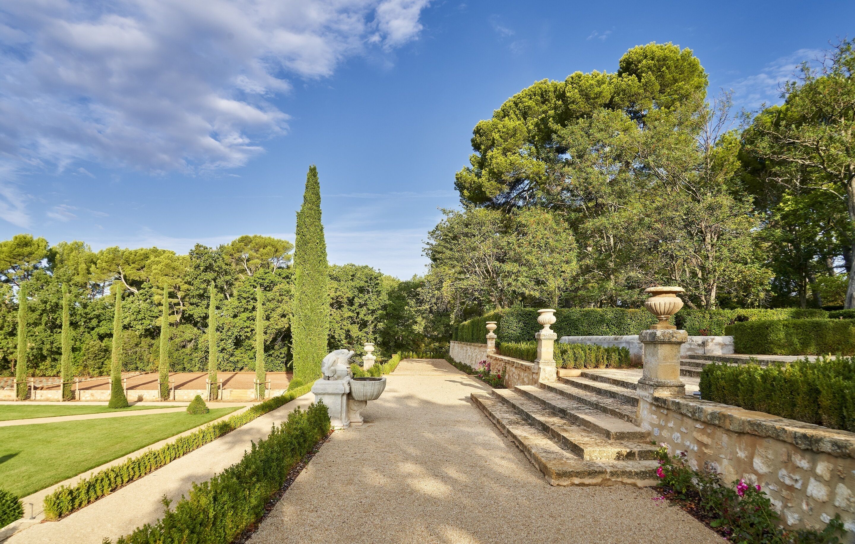 Un jardín formal con un sendero de grava, setos podados y estatuas clásicas.