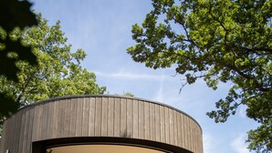 Una estructura moderna y circular de madera, con una cama, zona de estar y vistas al entorno verde.