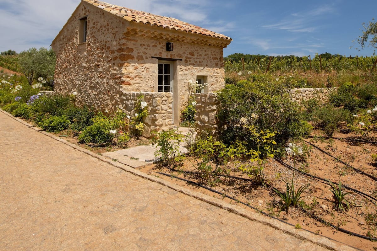 Ein Steinhhaus mit Ziegeldach, umgeben von einem Garten mit verschiedenen Pflanzen und Blumen.