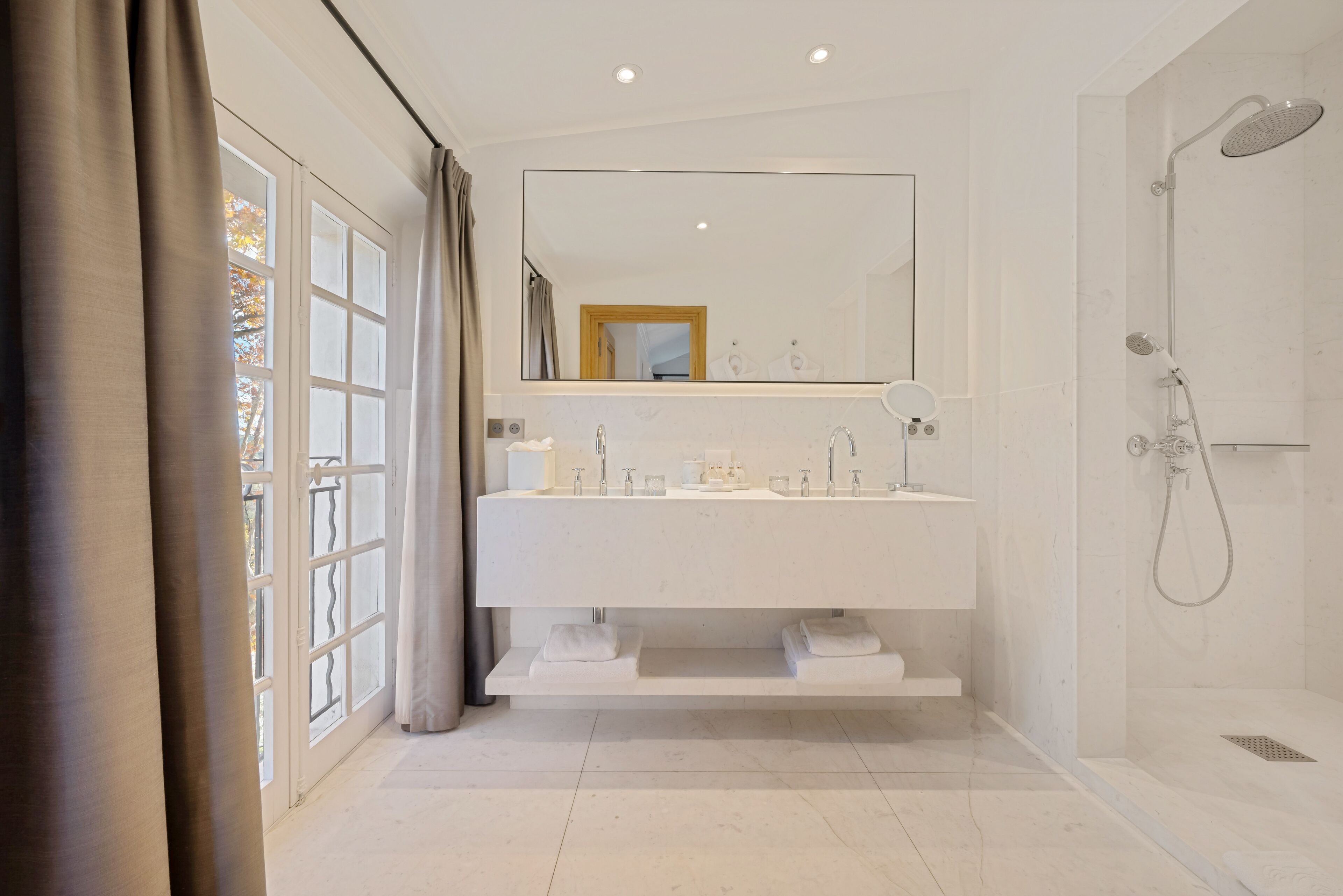 Une salle de bain moderne avec un grand miroir, une douche et une fenêtre avec des rideaux.