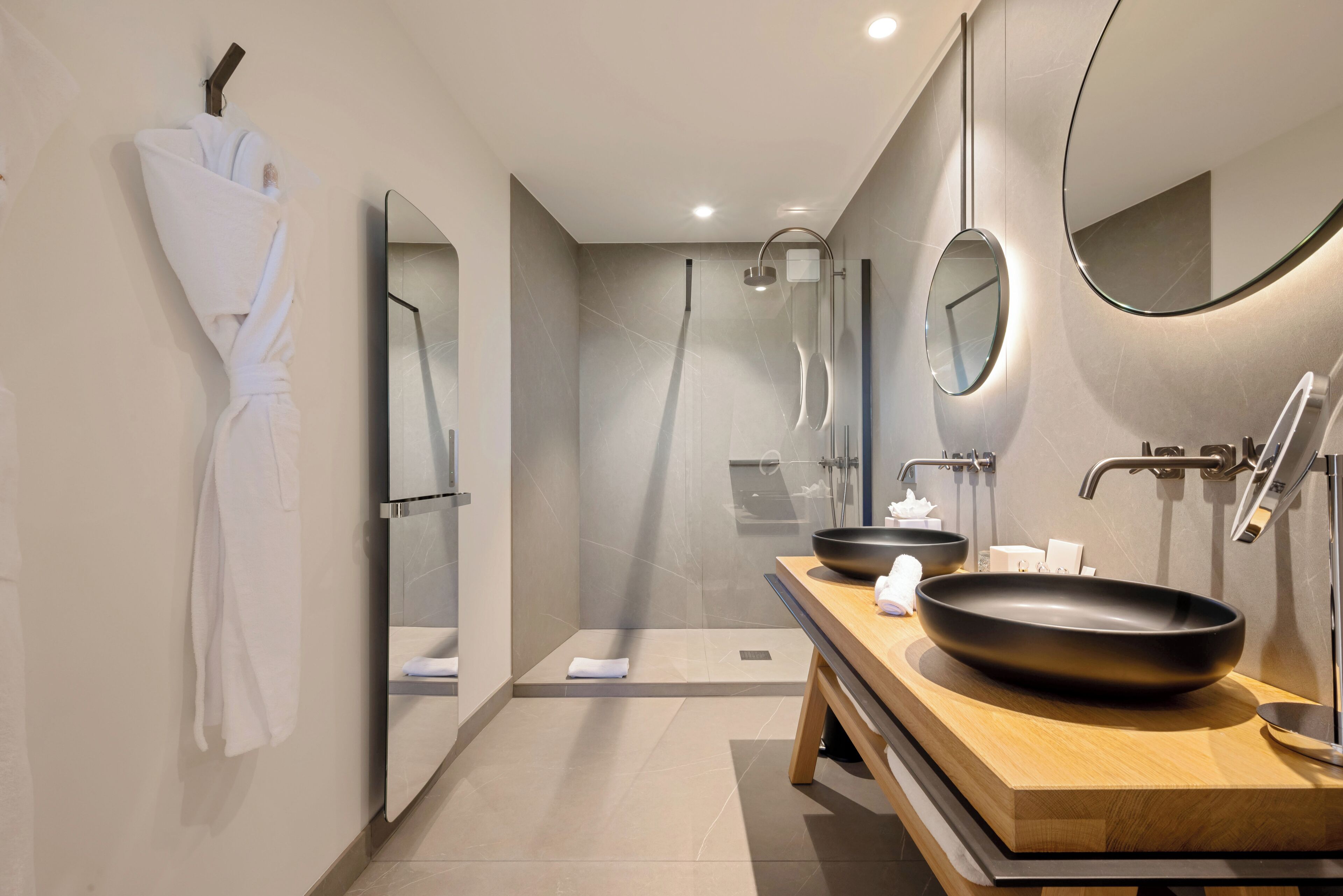 Un baño moderno con un espejo grande, un tocador de madera, un lavamanos negro y una zona de ducha.