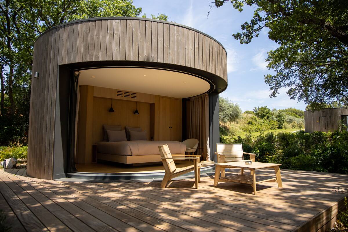 Eine moderne, runde Holzkonstruktion mit offener Innenarchitektur, ausgestattet mit einem Bett, einer Sitzecke und einem Tisch.