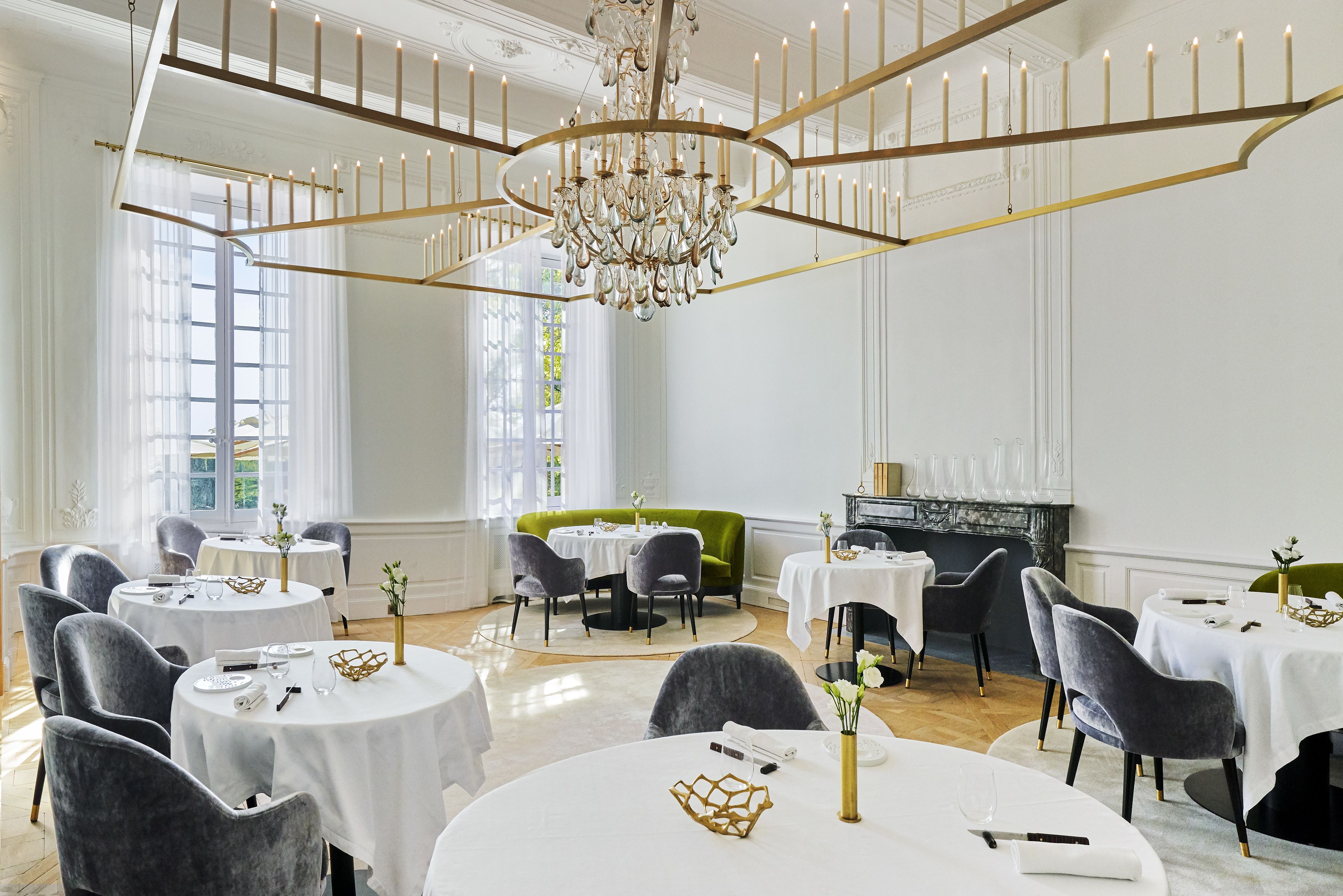 A dining area with round tables, grey upholstered chairs, and a chandelier.