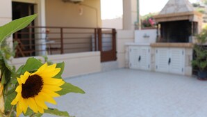 Un espace patio agrémenté d’un tournesol, d’un barbecue et d’une armoire blanche.