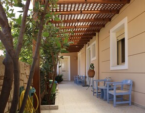 A covered outdoor corridor with a wooden pergola, potted plants, and blue chairs. - Helianthus (Malevizi)