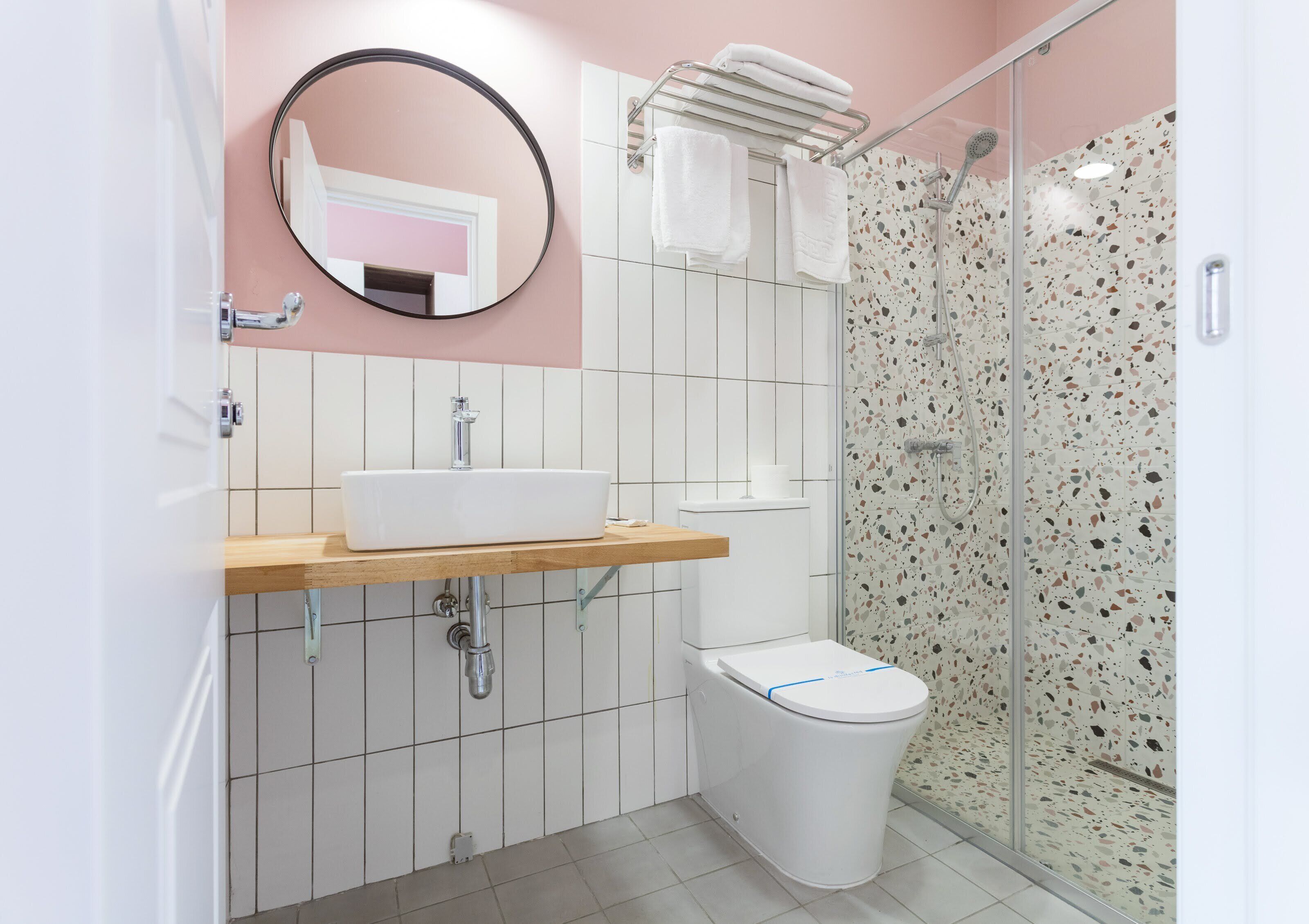 A modern bathroom with a white sink, a toilet, and a shower with a speckled tile wall.