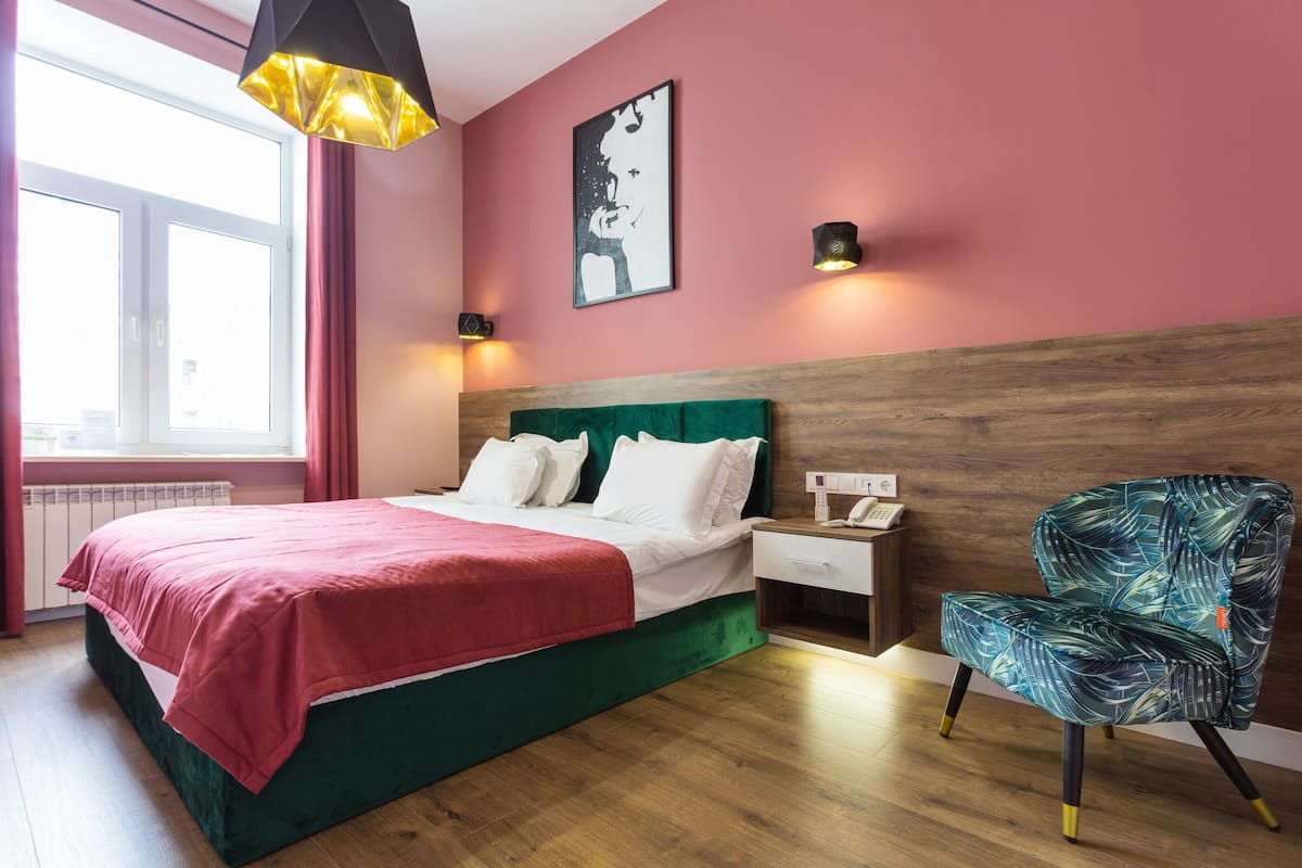 A bedroom with a bed, a nightstand, a chair, a window, and a wall art piece.