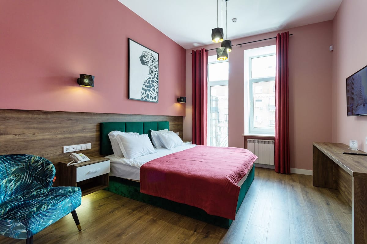 A hotel room with a bed, a desk, a chair, a nightstand, a telephone, and a window with curtains.