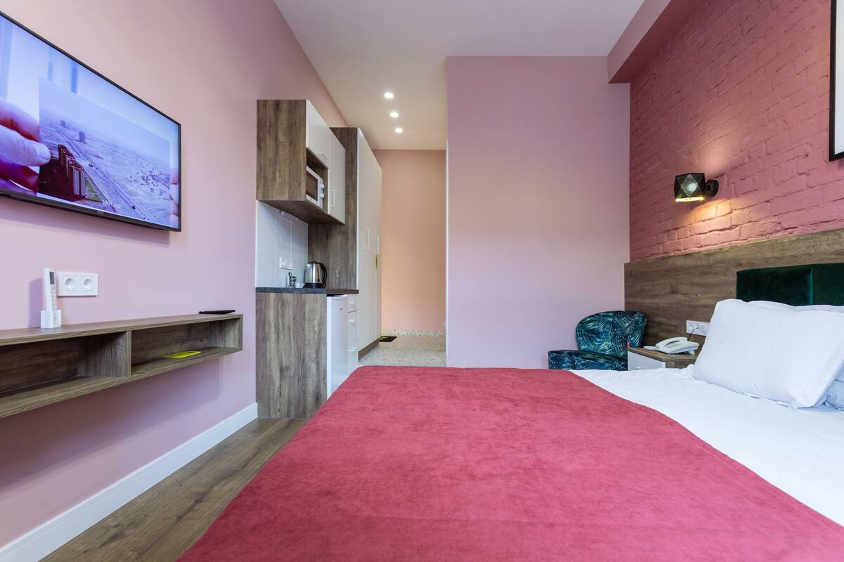 A modern hotel room with a large bed, a TV mounted on the wall, a wooden cabinet, and a brick accent wall.
