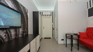 A modern hotel room with a flat-screen TV mounted on the wall, a red sofa, a small round table with a glass, and a door leading to another room. - Partner Guest House Velyka Vasylkivska (Kyiv)