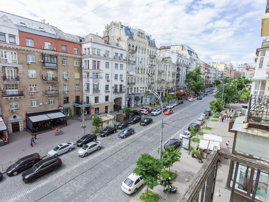 A street view of a city with multi-story buildings, parked cars, and pedestrians.