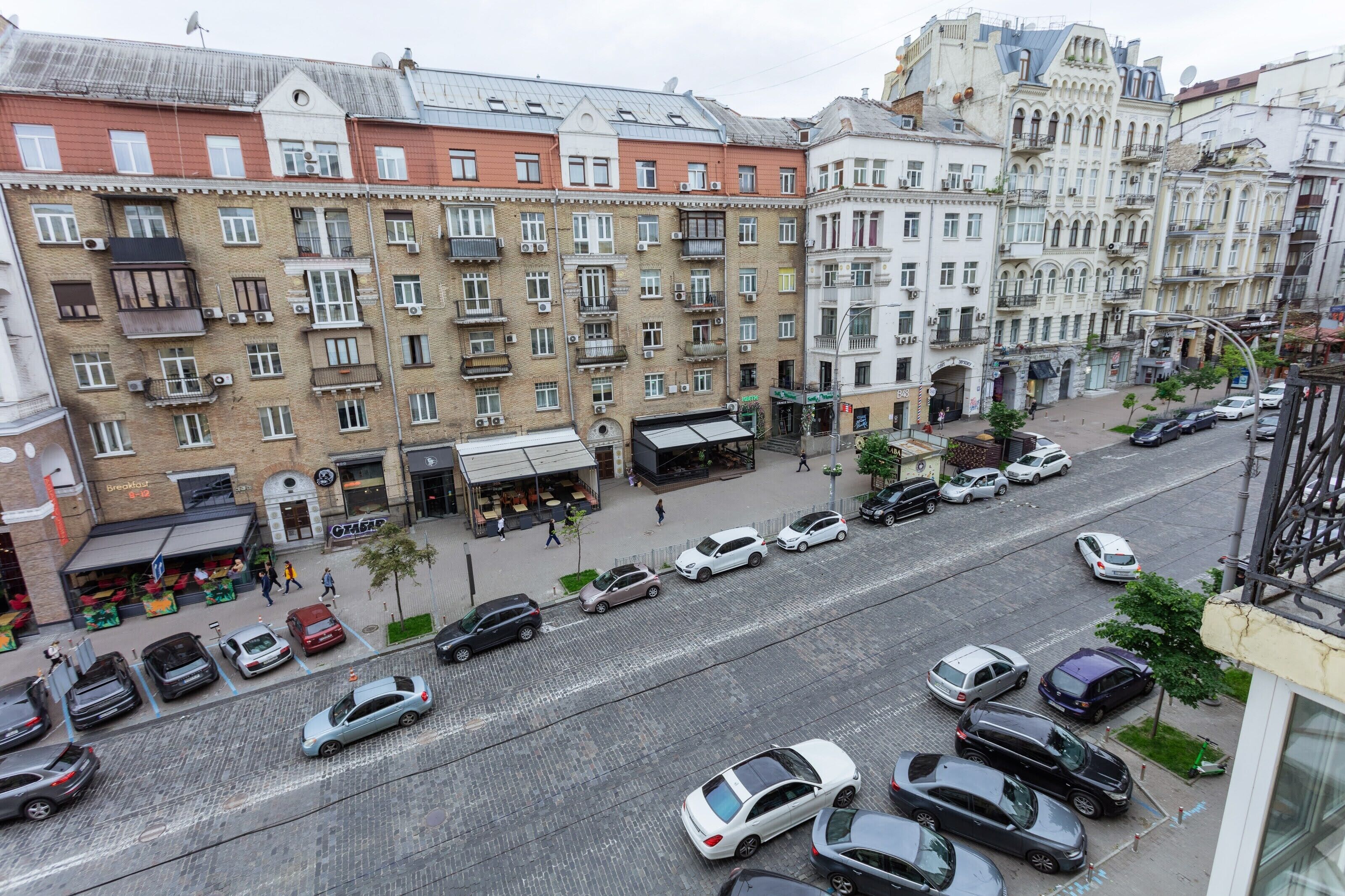 A street view with multi-story buildings, parked cars, and pedestrians.